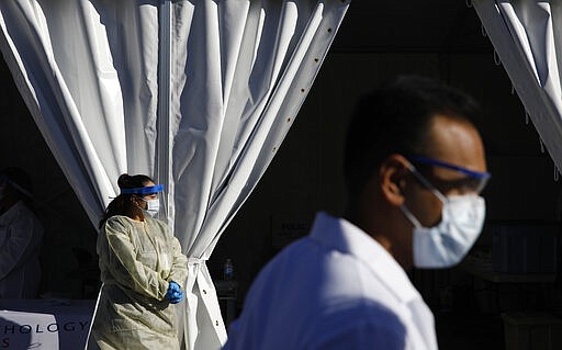 Health care workers with the UNLV School of Medicine wait in personal protective equipment for patients at a drive thru coronavirus testing site Tuesday, March 24, 2020, in Las Vegas. UNLV Medicine, the clinical arm of the UNLV School of Medicine, started conducting COVID-19 testing by appointment for people who meet the Centers for Disease Control and Prevention guidelines. (AP Photo/John Locher)