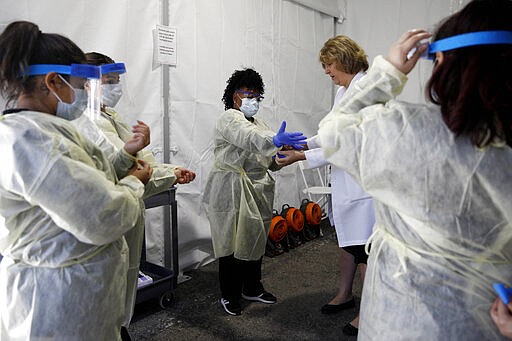 Doctors and healthcare workers with the University of Nevada, Las Vegas School of Medicine suit up in personal protective equipment before taking patients at a drive-through coronavirus testing site Tuesday, March 24, 2020, in Las Vegas. UNLV Medicine, the clinical arm of the UNLV School of Medicine, started conducting COVID-19 testing by appointment for people who meet the Centers for Disease Control and Prevention guidelines. (AP Photo/John Locher)