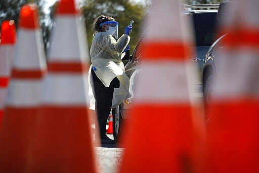 A healthcare worker with the University of Nevada, Las Vegas School of Medicine tests a patient for the coronavirus at a drive-through testing site Tuesday, March 24, 2020, in Las Vegas. UNLV Medicine, the clinical arm of the UNLV School of Medicine, started conducting COVID-19 testing by appointment for people who meet the Centers for Disease Control and Prevention guidelines. (AP Photo/John Locher)