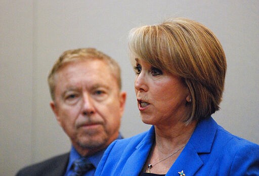 In this Wednesday, March 11, 2020, photo New Mexico Gov. Michelle Lujan Grisham, right, announces a public health emergency in response to the state's first positive tests for COVID-19, at a news conference in Santa Fe, N.M., also attended by Human Services Secretary David Scrase, left. Her administration has banned many gatherings of 100 or more people at spaces such as auditoriums and stadiums as a precaution against the spread of coronavirus. (AP Photo/Morgan Lee)