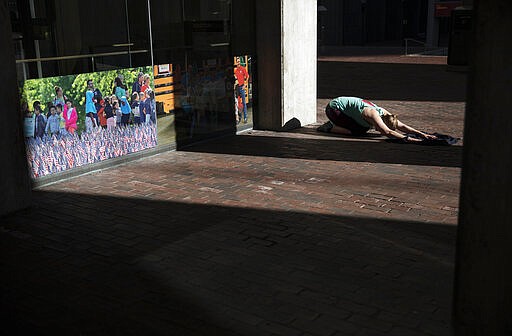 Unable to work out at her gym since it closed due to coronavirus, a woman stretches in a quiet corner while exercising at the entrance to City Hall, March 21, 2020, in Boston. (AP Photo/David Goldman)