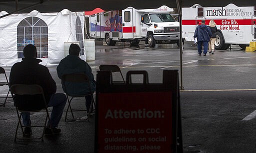 Seated in chairs set eight feet apart, blood donors wait to be taken to one of three mobile blood centers during a blood drive hosted by Marsh Regional Blood Center at the Bristol Motor Speedway Monday, March 23, 2020. With a nationwide shortage of blood supply growing, the blood drive provides local residents the opportunity to donate in a time of need due to the coronavirus pandemic. (David Crigger/Bristol Herald Courier via AP)