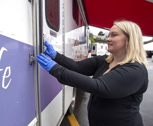 Alice Compton, with Marsh Regional Blood Center, sanitizes the a door handle of one of the blood mobiles after a blood donor leaves on Monday, March 23, 2020 from a blood drive at the Bristol Motor Speedway in Bristol, Tenn. With a nationwide shortage of blood supply growing, the blood drive provides local residents the opportunity to donate in a time of need due to the coronavirus pandemic. (David Crigger/Bristol Herald Courier via AP)