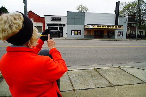 Linda Silber takes a photo of the encoring message on the marquee of the Rialto Theater in Raleigh, N.C., on Tuesday, March 24, 2020. Silber is part of a movie club that meets at the theater regularly, but it, like most other businesses, are closed due to the COVID-19 outbreak. (AP Photo/Allen G. Breed)