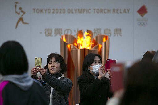 People take pictures with the Olympic Flame during a ceremony in Fukushima City, Japan, Tuesday, March 24, 2020. The Tokyo Olympic torch relay will start Thursday as planned in northeastern Fukushima prefecture, but with no torch, no torchbearers, no public, and little ceremony. (AP Photo/Jae C. Hong)