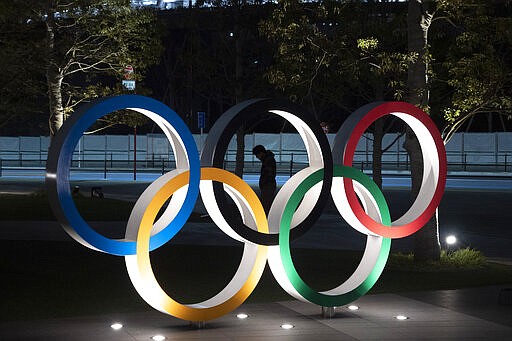 A man is seen through the Olympic rings in front of the New National Stadium in Tokyo, Tuesday, March 24, 2020. IOC President Thomas Bach has agreed &quot;100%&quot; to a proposal of postponing the Tokyo Olympics for about one year until 2021 because of the coronavirus outbreak, Japanese Prime Minister Shinzo Abe said Tuesday. (AP Photo/Jae C. Hong)