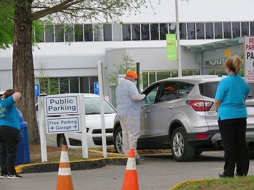 A worker in protective suit and mask talks to a driver who has been through the COVID-19 drive-through testing at West Jefferson Medical Center in Marrero, La., on Friday, March 20, 2020. The two women in blue T-shirts also are masked. A handful of cars and trucks went through the site early Friday. Most drove straight out but a couple were directed into this area. (AP Photo/ Janet McConnaughey)