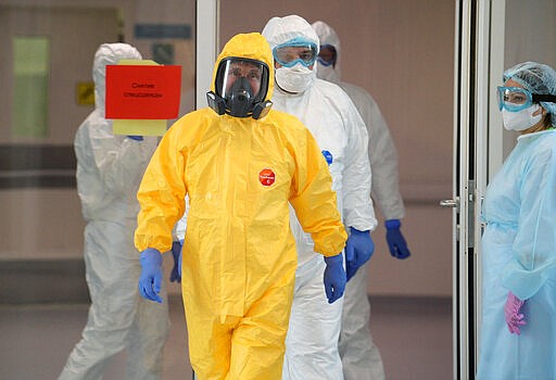 Russian President Vladimir Putin, center, wearing a protective suit enters a hall during his visit to the hospital for coronavirus patients in Kommunarka settlement, outside Moscow, Russia, Tuesday, March 24, 2020.  For some people the COVID-19 coronavirus causes mild or moderate symptoms, but for some it can cause severe illness including pneumonia. (Alexei Druzhinin, Sputnik, Kremlin Pool Photo via AP)