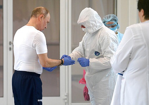 Russian President Vladimir Putin, left, dons gloves during his visit to the hospital for coronavirus patients in Kommunarka settlement, outside Moscow, Russia, Tuesday, March 24, 2020. Putin praised its doctors for high professionalism, saying they were working &quot;like clockwork.&quot;   For some people the COVID-19 coronavirus causes mild or moderate symptoms, but for some it can cause severe illness including pneumonia.(Alexei Druzhinin, Sputnik, Kremlin Pool Photo via AP)