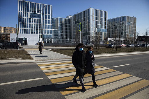 A couple wearing face masks cross the street in front of the hospital for coronavirus patients in Kommunarka settlement, outside Moscow, Russia, Tuesday, March 24, 2020, with Russia only reporting a few hundred virus cases. The highly contagious COVID-19 coronavirus can cause mild symptoms, but for some it can cause severe illness including pneumonia. (AP Photo/Pavel Golovkin)
