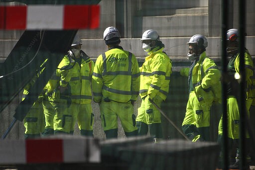 Construction workers wearing face masks seen through safety fencing work on a site near London Bridge in London, Tuesday, March 24, 2020. Britain's Prime Minister Boris Johnson on Monday imposed its most draconian peacetime restrictions due to the spread of the coronavirus on businesses and gatherings, health workers begged for more gear, saying they felt like &quot;cannon fodder.&quot; For most people, the new coronavirus causes only mild or moderate symptoms. For some it can cause more severe illness. (AP Photo/Alberto Pezzali)