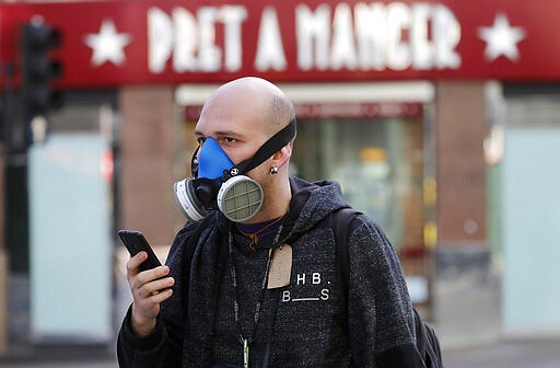 A man wears a mask as he walks through London, Tuesday, March 24, 2020. Britain's Prime Minister Boris Johnson on Monday imposed its most draconian peacetime restrictions due to the spread of the coronavirus on businesses and social gatherings.  For most people, the new coronavirus causes mild or moderate symptoms, but for some it can cause more severe illness. (AP Photo/Frank Augstein)