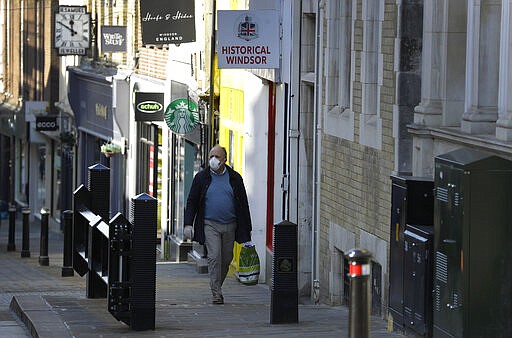 A shopper walks up an empty street near Windsor Castle in Windsor, England Tuesday, March 24, 2020. Britain's Prime Minister Boris Johnson on Monday imposed its most draconian peacetime restrictions due to the spread of the coronavirus on businesses and gatherings.  For most people, the new coronavirus causes only mild or moderate symptoms. For some it can cause more severe illness.(AP Photo/Kirsty Wigglesworth)