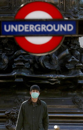 A man wears a face mask at the entrance of Piccadilly Circus tube station in London, Tuesday, March 24, 2020. Britain's Prime Minister Boris Johnson on Monday imposed its most draconian peacetime restrictions due to the spread of the coronavirus on businesses and social gatherings.  The highly contagious COVID-19 coronavirus can cause mild symptoms, but for some it can cause severe illness including pneumonia. (AP Photo/Frank Augstein)