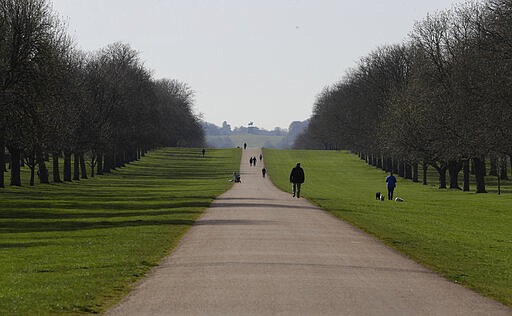 People keep a distance as they walk dogs on the Long Walk at Windsor Castle, England Tuesday, March 24, 2020. Britain's Prime Minister Boris Johnson on Monday imposed its most draconian peacetime restrictions due to the spread of the coronavirus on businesses and gatherings. For most people, the new coronavirus causes only mild or moderate symptoms. For some it can cause more severe illness. (AP Photo/Kirsty Wigglesworth)