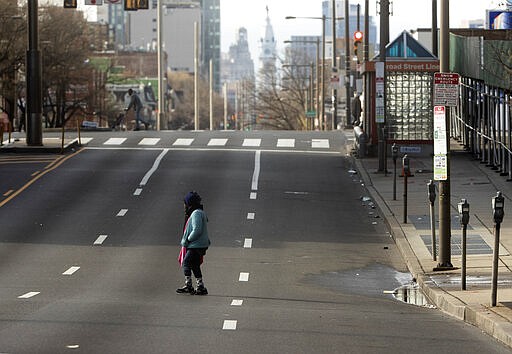 A person crosse North Broad Street in Philadelphia, which is deserted due to coronavirus fears Tuesday, March 24, 2020. (AP Photo/Matt Rourke)