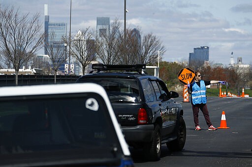 A healthcare worker directs cars at a COVID-19 testing site near Citizens Bank Park, home of the Philadelphia Phillies baseball team, Tuesday, March 24, 2020, in Philadelphia. For most people, the new coronavirus causes only mild or moderate symptoms. For some it can cause more severe illness. (AP Photo/Matt Slocum)