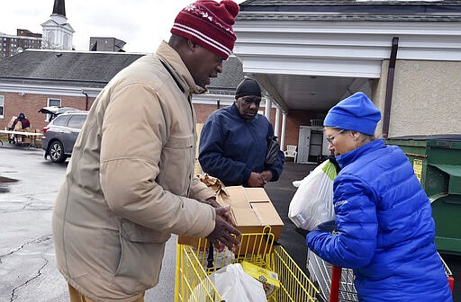 Maureen Pascal helps Ernest Taylor and Denise Phillips load a shopping cart with food at the Al Beech/West Side Food Pantry, Tuesday, March 24, 2020, in Kingston, Pa. Normally the pantry is set up like a store, but due to the coronavirus pandemic it is operating as a drive-thru pantry. (Aimee Dilger/The Times Leader via AP)