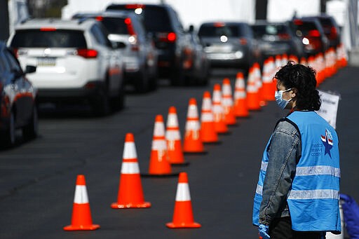 A healthcare worker directs cars at a COVID-19 testing site near Citizens Bank Park, home of the Philadelphia Phillies baseball team, Tuesday, March 24, 2020, in Philadelphia. For most people, the new coronavirus causes only mild or moderate symptoms. For some it can cause more severe illness. (AP Photo/Matt Slocum)