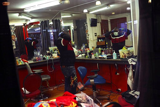 A hairdresser puts on his protective mask in front of a mirror prior to cutting a client's hair at a hair salon in the Matonge Quarter of Brussels, Monday, March 23, 2020. After Belgian Prime Minister Sophie Wilmes announced that hairdressers would still be able to operate, while many other stores were required to be closed during the coronavirus epidemic, some thought it was a bad Belgian joke. Fearing for their health, some hairdressers now are calling on the government to order the closure of all salons without delay. For most people, the new coronavirus causes only mild or moderate symptoms, such as fever and cough. For some, especially older adults and people with existing health problems, it can cause more severe illness, including pneumonia. (AP Photo/Francisco Seco)