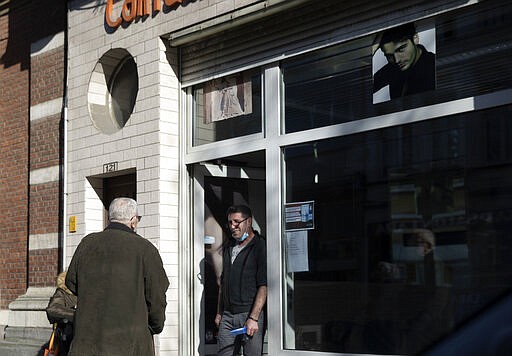 A barber wearing a mouth mask speaks with a client outside his shop in Antwerp, Belgium, Monday, March 23, 2020. After Belgian Prime Minister Sophie Wilmes announced that hairdressers would still be able to operate, while many other stores were required to be closed during the coronavirus epidemic, some thought it was a bad Belgian joke. Fearing for their health, some hairdressers now are calling on the government to order the closure of all salons without delay. For most people, the new coronavirus causes only mild or moderate symptoms, such as fever and cough. For some, especially older adults and people with existing health problems, it can cause more severe illness, including pneumonia. (AP Photo/Virginia Mayo)