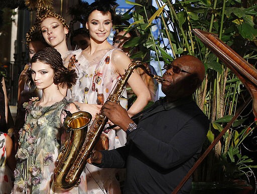 FILE - In this Jan.24, 2018 file photo, models present creations for Franck Sorbier's Haute Couture Spring-Summer 2018 fashion collection while saxophonist Manu Dibango performs in Paris. Renowned jazz man Manu Dibango, to many the beloved &quot;Papy Groove&quot; who served as an inspiration and pioneer in his art, died on Tuesday from the coronavirus, his official Facebook page announced. He was 86. For most people, the new coronavirus causes only mild or moderate symptoms. For some it can cause more severe illness. (AP Photo/Christophe Ena, File)