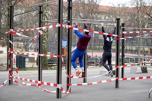 Two men exercise at a free public gym cordoned off with barrier tape in the Volkspark Wilmersdorf in Berlin, Germany, March 20, 2020. (Christoph Soeder/dpa via AP)