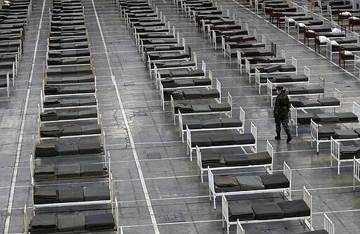 A Serbian soldier inspects beds for treatment of possible COVID-19 infected patients inside of the Belgrade Fair, Serbia, Tuesday, March 24, 2020. For most people, the new coronavirus causes only mild or moderate symptoms. For some it can cause more severe illness. (AP Photo/Darko Vojinovic)