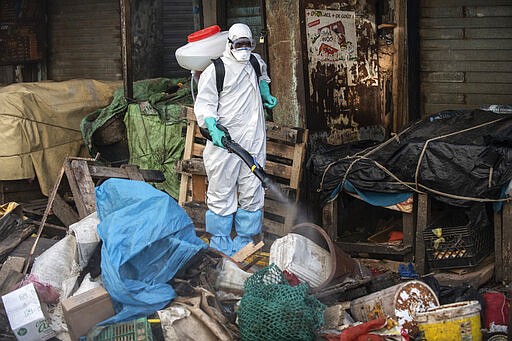 In this photograph taken Sunday March 22, 2020, a municipal worker sanitizes the street of Dakar's popular Medina's neighborhood after a bulldozer demolished informal shops in an effort to stop the spread of the coronavirus. For most people the virus causes only mild or moderate symptoms. For others it can cause more severe illness, especially in older adults and people with existing health problems. (AP Photo/Sylvain Cherkaoui)