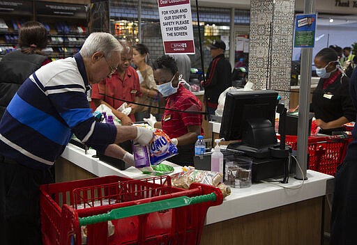 A screen divides a cashier, left, and customer right, at a pay point in a Spar supermarket,  in Johannesburg, Tuesday, March 24, 2020, the day after it was announced that South Africa will go into a nationwide lockdown for 21 days from Thursday to fight the spread of the new coronavirus. For most people the virus causes only mild or moderate symptoms . For others it can cause more severe illness, especially in older adults and people with existing health problems. (AP Photo/Denis Farrell)