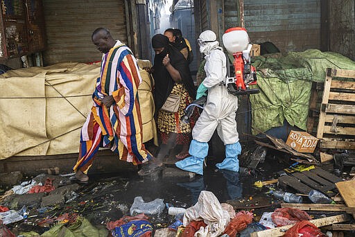 In this photograph taken Sunday March 22, 2020, a municipal worker sanitizes the street of Dakar's popular Medina's neighborhood after a bulldozer demolished informal shops in an effort to stop the spread of the coronavirus. For most people the virus causes only mild or moderate symptoms. For others it can cause more severe illness, especially in older adults and people with existing health problems. (AP Photo/Sylvain Cherkaoui)