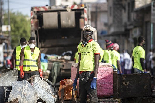 In this photograph taken Sunday March 22, 2020, municipal workers block the streets of Dakar's popular Medina's neighborhood as a bulldozer demolishes informal shops in an effort to stop the spread of the coronavirus. For most people the virus causes only mild or moderate symptoms. For others it can cause more severe illness, especially in older adults and people with existing health problems. (AP Photo/Sylvain Cherkaoui)