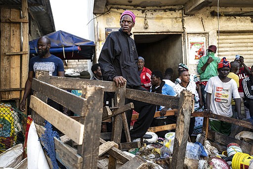 In this photograph taken Sunday March 22, 2020, a a shopkeeper looks on in Dakar's popular Medina's neighborhood as a bulldozer demolishes informal shops in an effort to stop the spread of the coronavirus. For most people the virus causes only mild or moderate symptoms. For others it can cause more severe illness, especially in older adults and people with existing health problems. (AP Photo/Sylvain Cherkaoui)