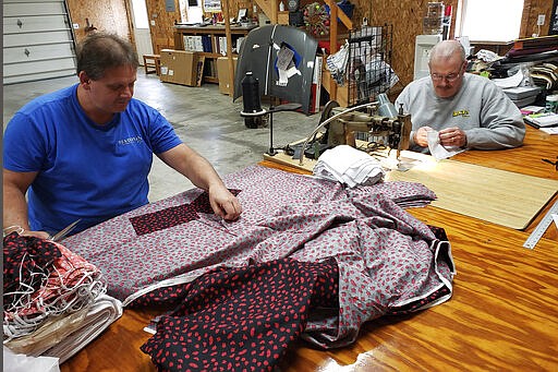 In this Sunday, March 22, 2020 photo, Bill Purdue, left, cuts pieces of fabric while Mike Rice sews them into face masks in Rice's autobody and upholstery shop in Washington, Ind. They will deliver the masks this week to Deaconess Health System in Evansville, Indiana, which asked community members to sew cloth masks for health care workers who may face a shortage amid the coronavirus pandemic. They're among legions of everyday Americans making face masks for desperate hospitals, nursing homes and homeless shelters that could run out of personal protective equipment.(photo courtesy of Robin Rice via AP)