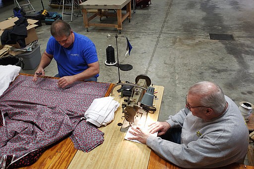 In this Sunday, March 22, 2020 photo, Bill Purdue, left, cuts pieces of fabric while Mike Rice sews them into face masks in Rice's autobody and upholstery shop in Washington, Ind. They will deliver the masks this week to Deaconess Health System in Evansville, Indiana, which asked community members to sew cloth masks for health care workers who may face a shortage amid the coronavirus pandemic. They're among legions of everyday Americans making face masks for desperate hospitals, nursing homes and homeless shelters that could run out of personal protective equipment.(photo courtesy of Robin Rice via AP)