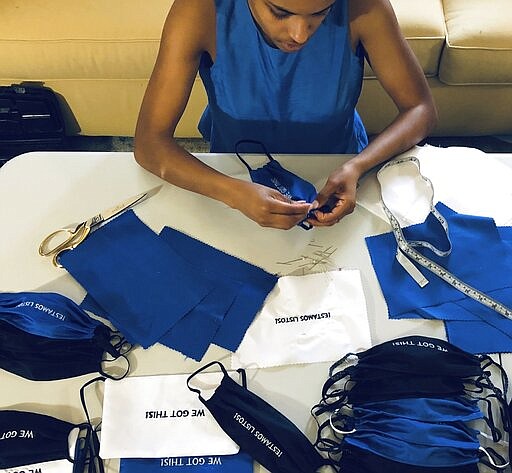 In this Sunday, March 22, 2020, photo, provided by Christina Hunter, Briana Danyele sews cloth face masks that say &quot;We Got This!&quot; in her mother's living room in Greer, S.C., which will be sent to health care workers. Legions of everyday Americans are sewing masks for desperate hospitals, nursing homes and homeless shelters amid the expanding coronavirus pandemic. (Christina Hunter via AP)