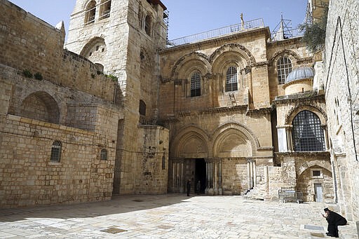 An Orthodox Christian priest checks his phone at an empty plaza in front to the Church of the Holy Sepluchre, where Christians believe Jesus Christ was buried, in Jerusalem, Monday, March 23, 2020. In Israel daily life has largely shut down with coronavirus cases multiplying greatly over the past week, (AP Photo/Mahmoud Illean)