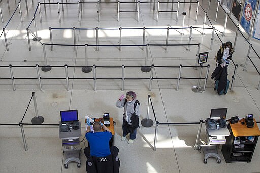 A passenger removes her goggles and face mask used to fend off coronavirus at the request of a TSA agent as she goes through a security checkpoint, Tuesday, March 24, 2020, at JFK airport in New York. (AP Photo/Mary Altaffer)