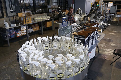 Tattersall Distilling co-founder Dan Oskey, back center, puts 32-oz bottles of newly made hand sanitizer on a conveyor belt for packaging Tuesday, March 24, 2020 in Minneapolis as the company lent a hand to provide the sanitizer, made from a World Health Organization recipe and signed off by the FDA and state licensing requirements to make available for nursing homes, health centers and first responders fighting the coronavirus. (AP Photo/Jim Mone)