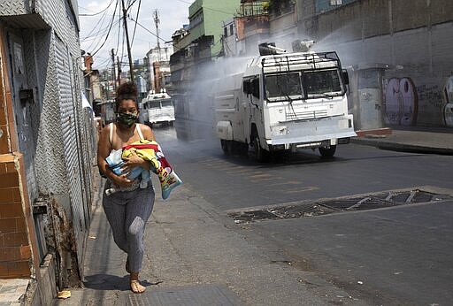 A woman runs carrying her baby as a Bolivarian National Guard water cannon sprays disinfectant as a preventive measure against the spread of the new coronavirus. in the Catia parish in Caracas, Venezuela, Tuesday, March 24, 2020.  President Nicolas Maduro has ordered the entire nation to stay home under a quarantine aimed at cutting off the spread of the new virus, calling it a &#147;drastic and necessary measure.&#148; (AP Photo/Ariana Cubillos)