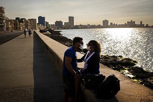 A couple wearing masks as a precaution against the spread of the new coronavirus, spend the afternoon at the malecon in Havana, Cuba, Monday, March 23, 2020. The vast majority of people recover from the COVID-19 disease. (AP Photo/Ramon Espinosa)