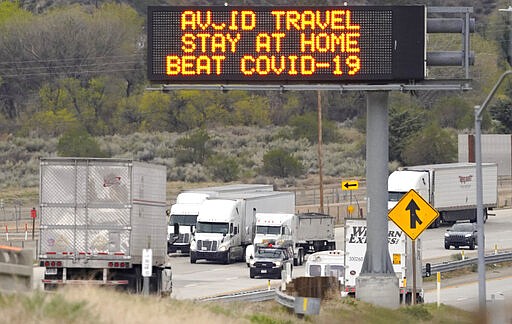 Semi trucks drive by a freeway sign along Interstate 5 that urges people to stay at home due to the COVID-19 outbreak on their way toward Los Angles, Tuesday, March 24, 2020, in Gorman, Calif. (AP Photo/Mark J. Terrill)