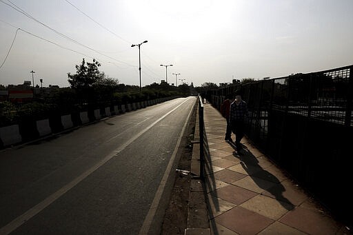 Indians walk wearing face masks on the side of an empty street during a lockdown amid concerns over the spread of Coronavirus, in New Delhi, India, Monday, March 23, 2020. Authorities have gradually started to shutdown much of the country of 1.3 billion people to contain the outbreak. For most people, the new coronavirus causes only mild or moderate symptoms. For some it can cause more severe illness. (AP Photo/Manish Swarup)