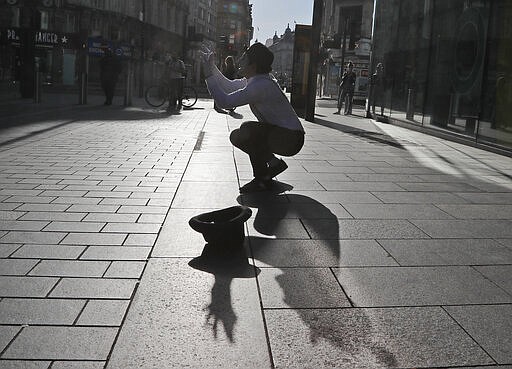 A street artist is watched by only a few people as he performs in London, Tuesday, March 24, 2020. Britain's Prime Minister Boris Johnson on Monday imposed its most draconian peacetime restrictions due to the spread of the coronavirus on businesses and social gatherings. The highly contagious COVID-19 coronavirus can cause mild symptoms, but for some it can cause severe illness including pneumonia. (AP Photo/Frank Augstein)