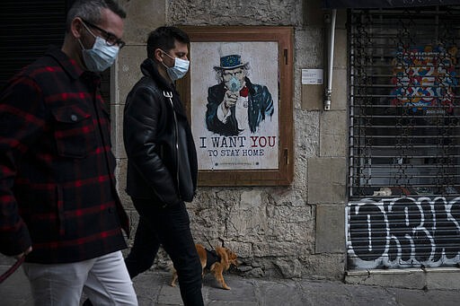 People walk past a poster that reads 'I want you to stay home', by artist TvBoy amid a lockdown in Barcelona, Spain, Tuesday, March 24, 2020. More than 1.5 billion around the world have been told to stay in their homes. For most people, the new coronavirus causes only mild or moderate symptoms. For some it can cause a more serious illness. (AP Photo/Felipe Dana)