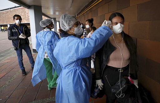 A nurse takes the temperature of a woman, outside the main bus terminal in Bogota, Colombia, Tuesday, March 24, 2020. The government announced a nationwide lockdown starting Tuesday to fight the spread of new coronavirus, putting strict restrictions on residents' movements, but emphasized it will guarantee the continuation of local agriculture and food distribution. (AP Photo/Fernando Vergara)