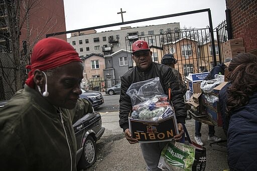 Surrounded by a few volunteers, a man carries food donations from St. Stephen Outreach in the Brooklyn borough of New York, on Friday, March 20, 2020. For decades, American nonprofits have relied on a cadre of volunteers who quite suddenly aren't able to show up. With millions staying home during the pandemic, charities that help the country's neediest are facing even greater need. Many Americans have now been ordered to shelter in place, but there is an exception for people providing essential services, and that includes food bank volunteering. (AP Photo/Wong Maye-E)