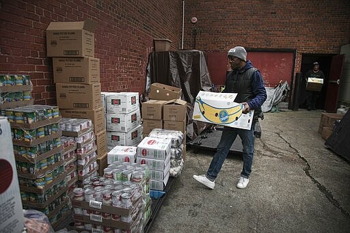 Rahim, a volunteer at the St. Stephen Outreach, carries food donations as he prepares to hand out food in the Brooklyn borough of New York, on Friday, March 20, 2020. For decades, American nonprofits have relied on a cadre of volunteers who quite suddenly aren't able to show up. With millions staying home during the pandemic, charities that help the country's neediest are facing even greater need. Many Americans have now been ordered to shelter in place, but there is an exception for people providing essential services, and that includes food bank volunteering. (AP Photo/Wong Maye-E)