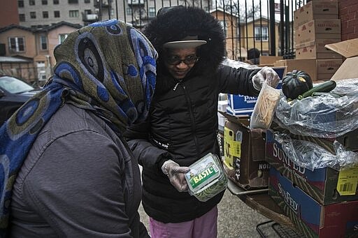 Elaine Peoples 68, right, gives out food donations to a woman at St. Stephen Outreach in the Brooklyn borough of New York, on Friday, March 20, 2020. For more than a week, Elaine Peoples, who cooked for a now-shuttered daycare center, has been out of work. At 68, she's also at higher risk for catching the novel coronavirus. Nonetheless she's showing up 4 days a week for her volunteer shift at an increasingly crowded Brooklyn soup kitchen and food pantry. (AP Photo/Wong Maye-E)