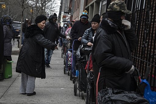 Sheila Williams, left, who manages the soup kitchen and food pantry at St. Stephen Outreach, tells people waiting in line for their food donations to keep bigger distances between one another, in the Brooklyn borough of New York, on Friday, March 20, 2020. Williams usually has 25 volunteers to feed about 100 people a day at St. Stephen Outreach in Brooklyn. Now she's down to just 10 volunteers and says that there are more people waiting in line for food. (AP Photo/Wong Maye-E)